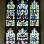 large chancel stained glass window showing jesus on the cross and saints surrounded by angels