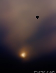 hot air balloon rising above setting sun