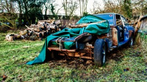 old wrecked sports car in a field with logs on it