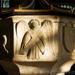 markings on stone font featuring lamb of god angel and shield